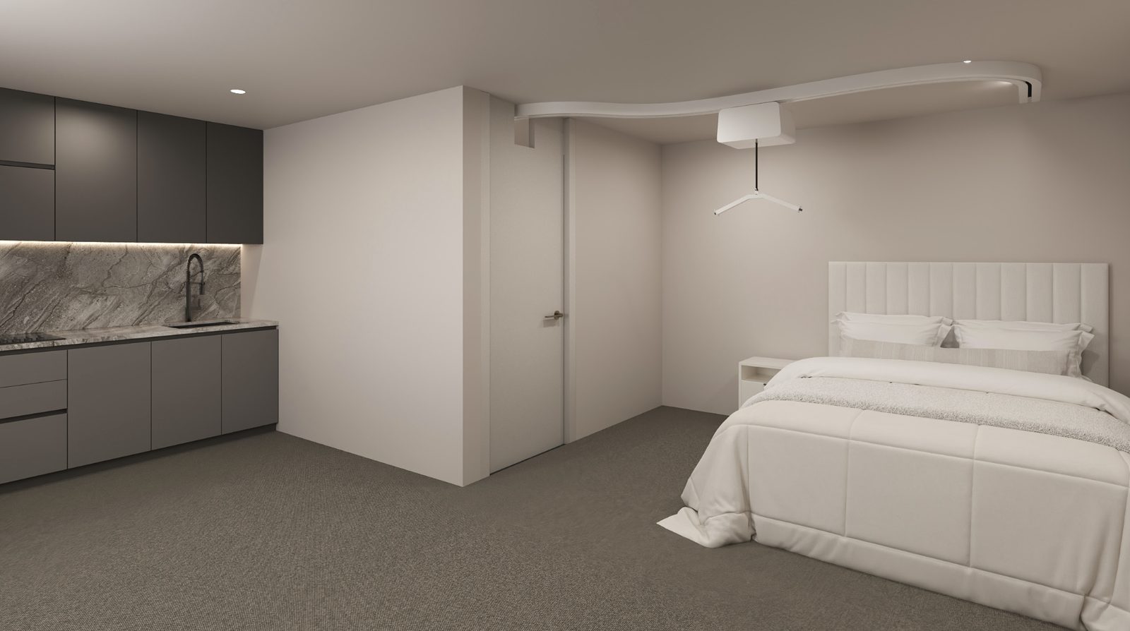 A studio flat with a dark grey fitted kitchen, stone splashback and a double bed with an upholstered headboard.